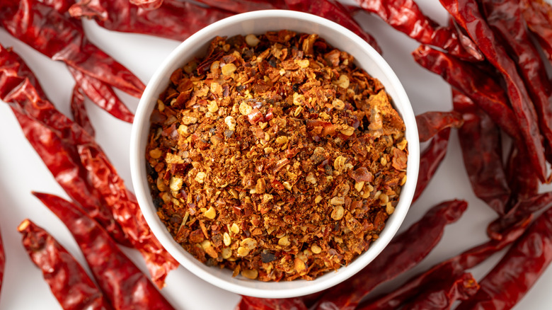 Dish of crushed red pepper flakes surrounded by dried chili peppers