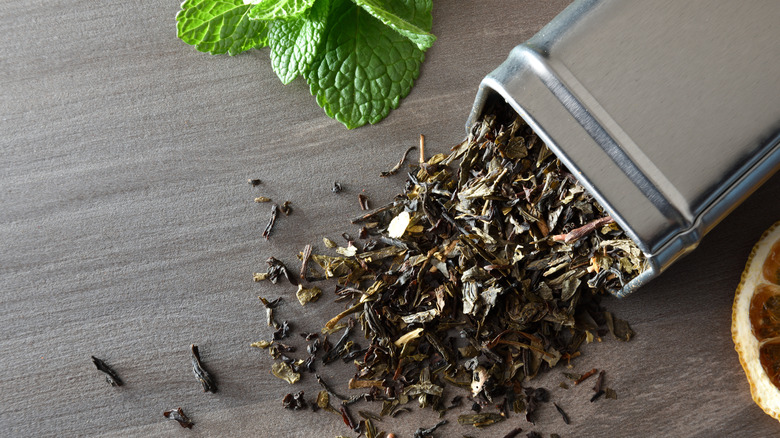 Green tea leaves spilling out from a metal tea cannister
