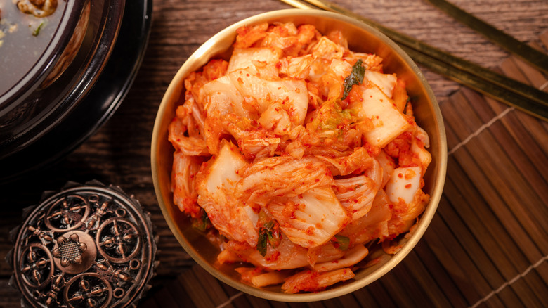 A bowl full of kimchi with chopsticks, a bowl of food and other items on the table.