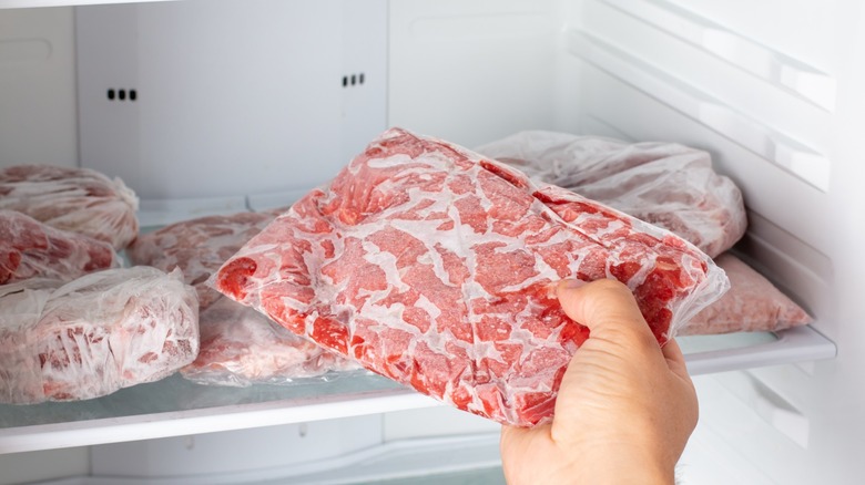 a hand taking a bag of frozen beef from a freezer of frozen meat