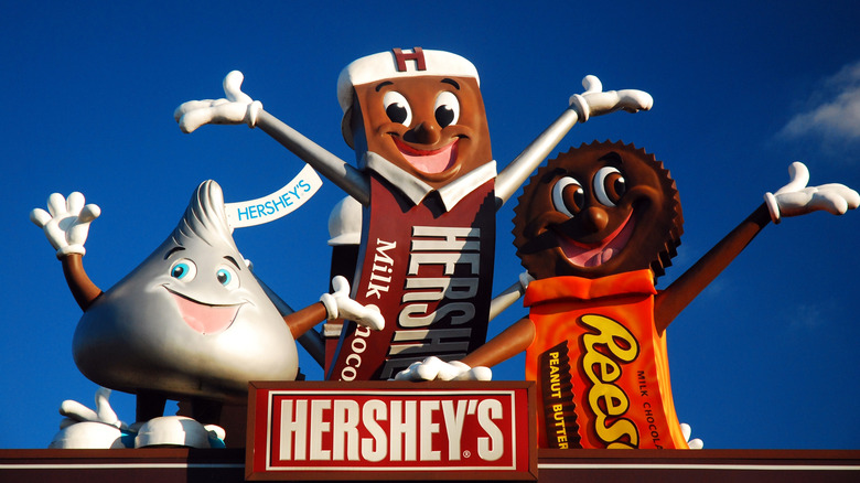 A sign from Hersheyland displaying cartoon versions of a Hershey's Kiss, a Hershey's Chocolate Bar, and Reese's Cups