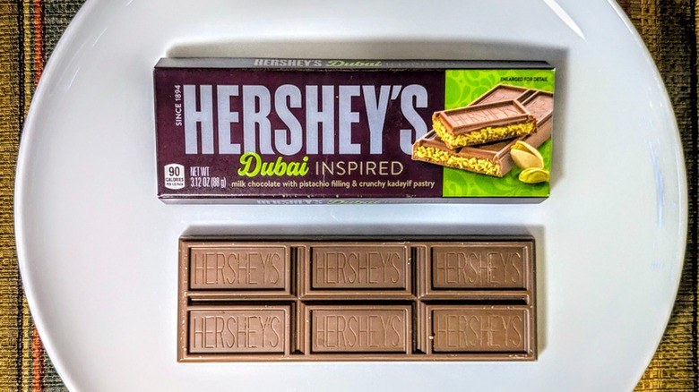 A Hershey's Dubai-Inspired Chocolate Bar in its box next to an unwrapped bar on a white plate