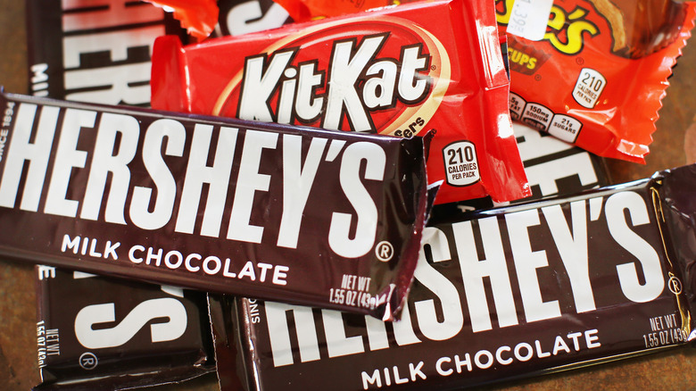 A pile of Hershey bars including Hershey milk chocolate, Kit Kat, and Reese's Peanut Butter Cups
