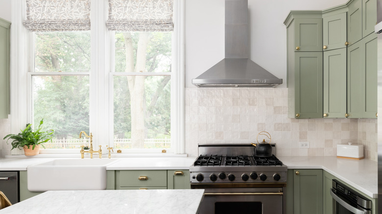 White kitchen with pale olive green cabinets and two tall windows