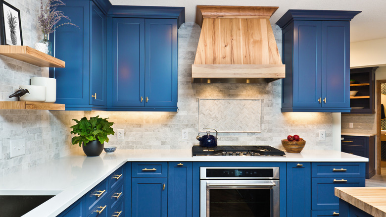 Kitchen with ocean blue cabinets and white counters with wood shelves and range hood