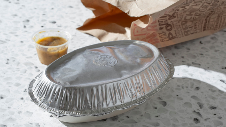 A closed Chipotle bowl beside a bag and a cup of sauce