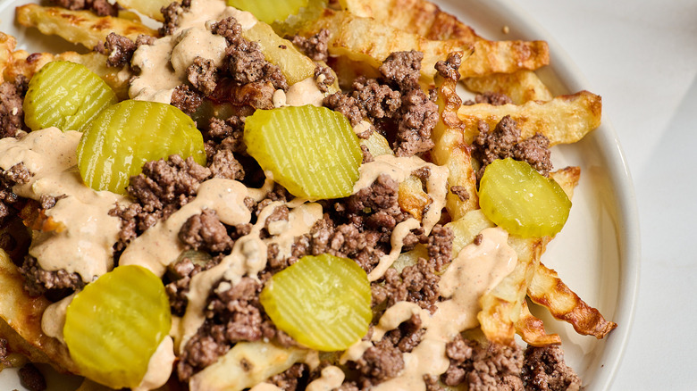close up of a plate of french fries with beef and pickles