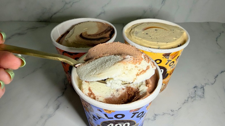 Hand holding spoonful of Halo Top ice cream over three pints of ice cream on marble surface