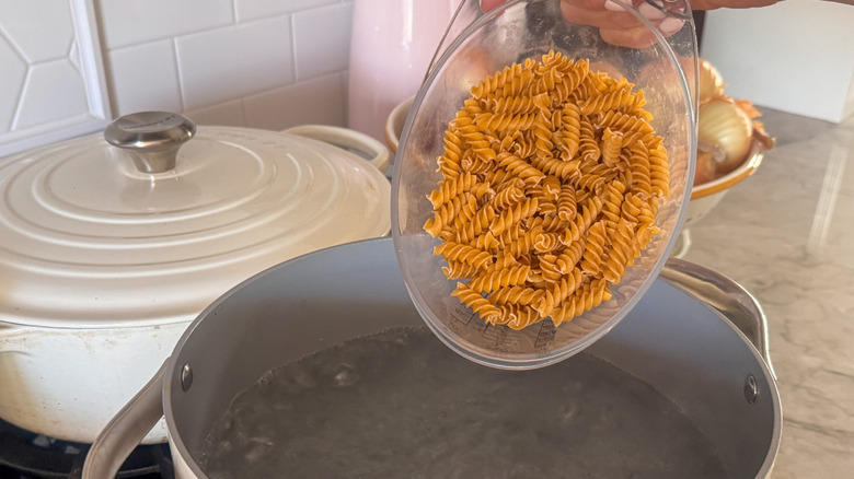 hand pouring pasta into pot