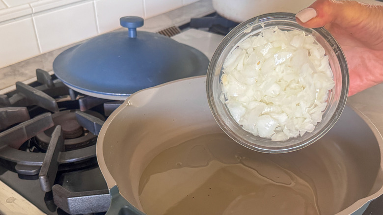 hand adding onion to pan