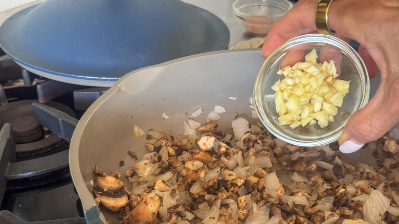 hand adding garlic to pan