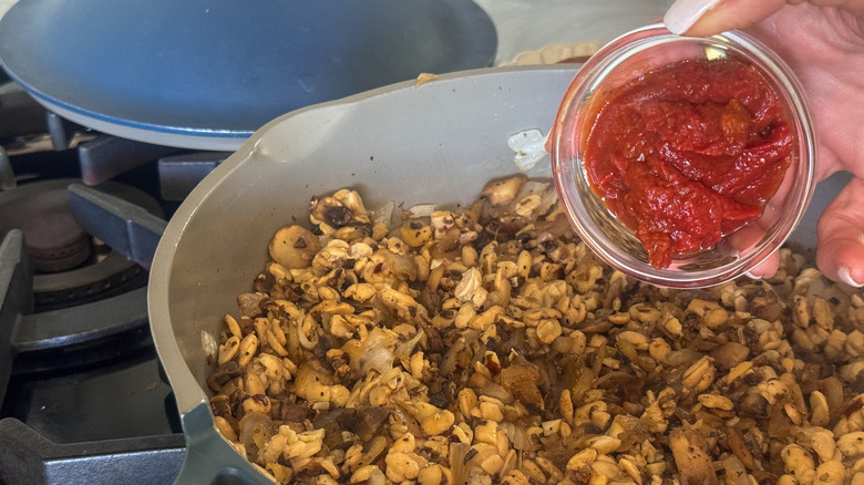 hand adding tomato paste