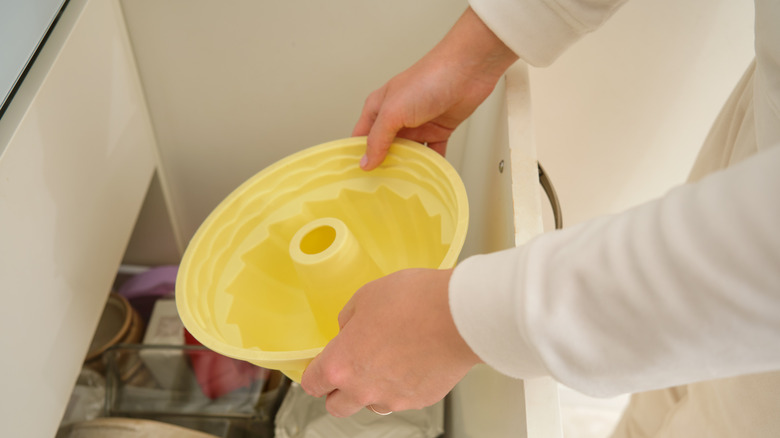 A person storing a yellow silicone Bundt pan in a kitchen drawer