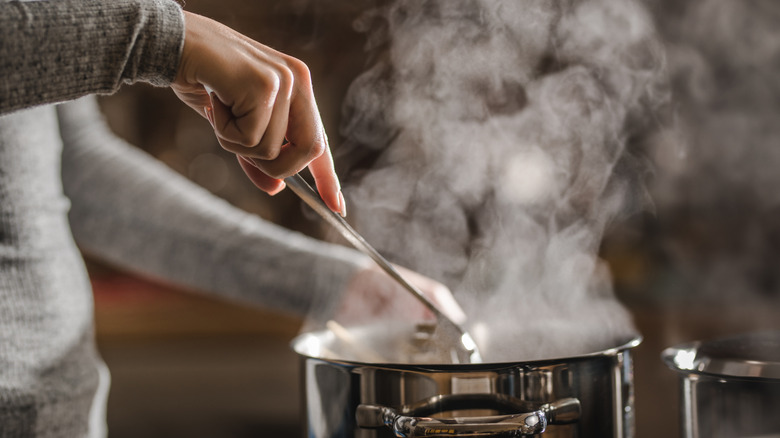 Woman's hands stirring pot of boiling water on stove