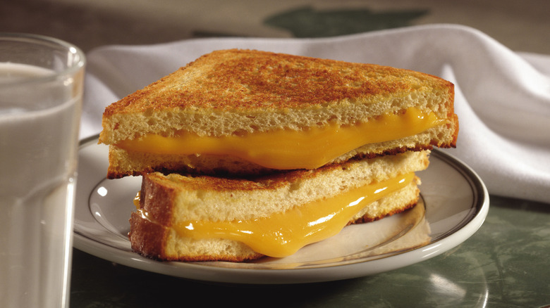 grilled cheese sandwich on a white plate with napkin and glass of milk