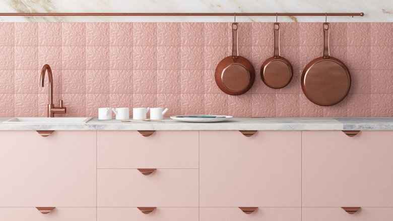 Pink kitchen with copper accents, copper pans hanging on wall