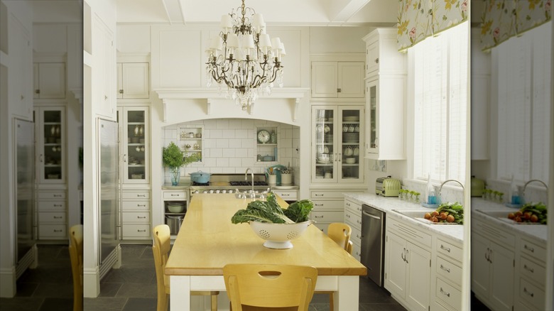 White kitchen with light wood table and chairs, large crystal chandelier, vintage accents on countertops