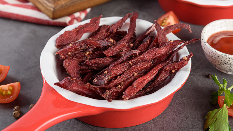 homemade beef jerky in white and red dish with sauce on the side