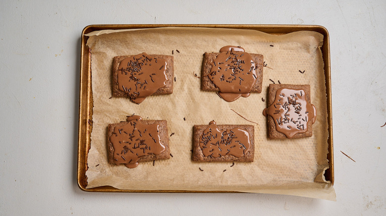 adding icing and sprinkles to pop tarts on sheet tray