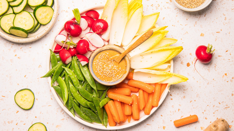 Sesame dressing in small bowl with vegetables all around.