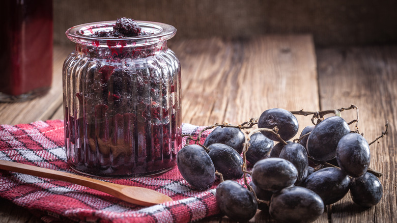 A jar of grape jelly with a bunch of grapes on the side