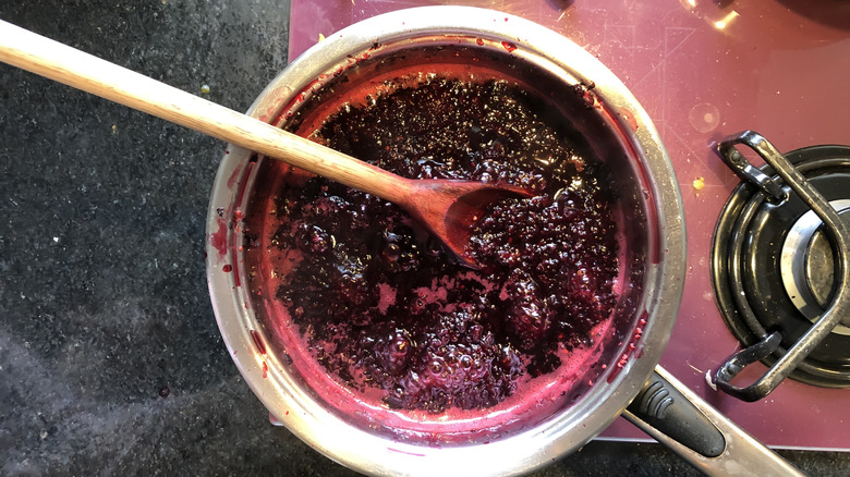A pan of hot fruit on a stove with a wooden spoon