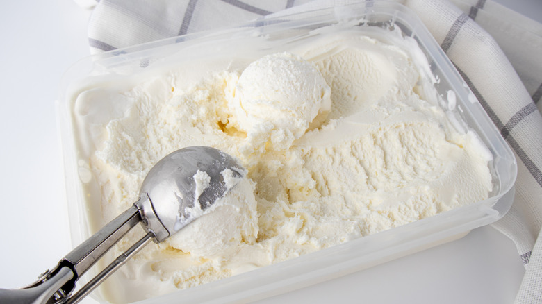 Vanilla ice cream is being scooped out of a tub.