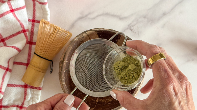 hand adding matcha to strainer