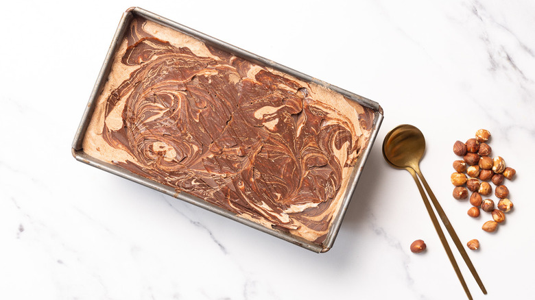 Nutella ice cream in container next to spoons and hazelnuts