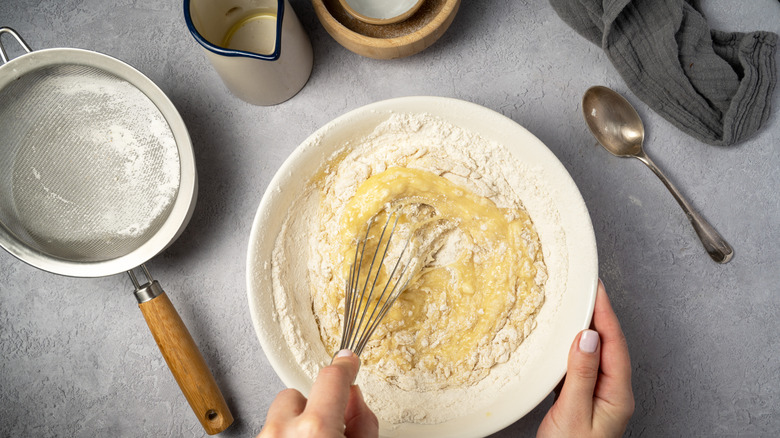 Hand mixing pancake batter in a bowl with a whisk next to kitchen equipment