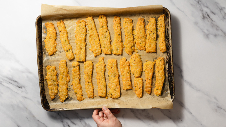 Hand holding baking sheet with baked cheese straws