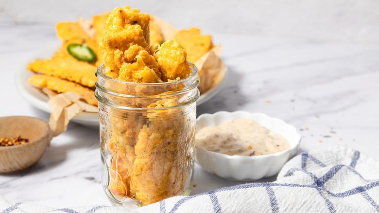 Baked spicy cheese straws in small jar with platter and smoked aioli in background