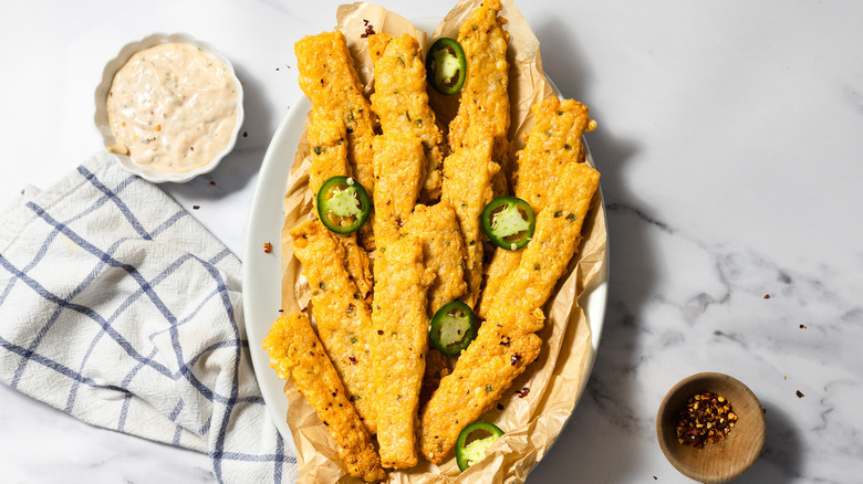 Baked spicy cheese straws on platter beside chili flakes and smoked aioli