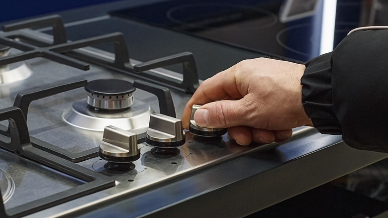Close-up of a human hand turning a knob and lighting the burner on a gas stove