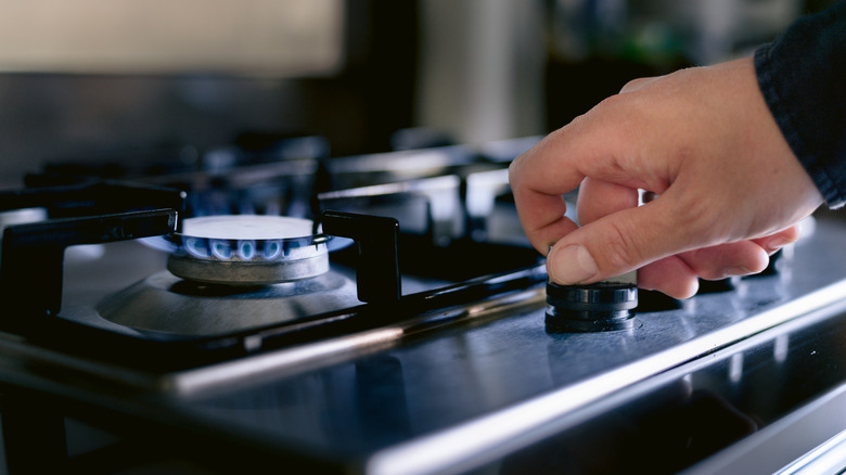 A hand turns on a stove fired by natural gas