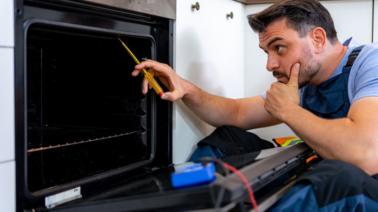 A technician inspects an oven with tools