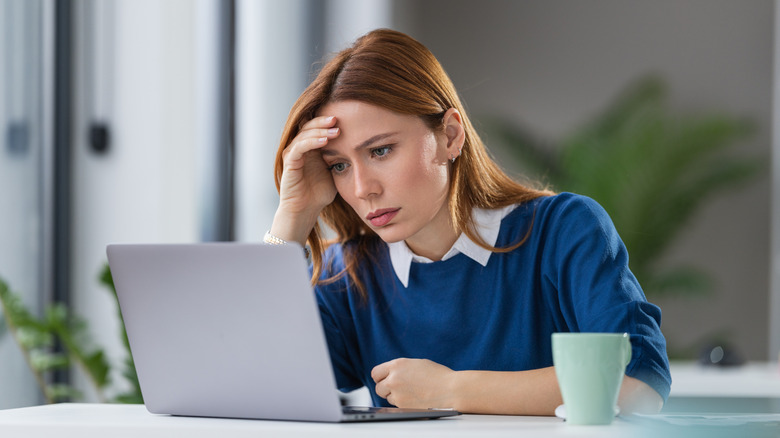 Young woman on a laptop appearing frustrated and tired
