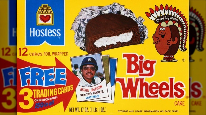 A 1970s era box of Ding Dongs featuring an image of a chocolate cake full of white cream sitting on foil next to a cartoon version of the cake dress like a king and an image in the bottom left of some baseball cards advertising three free cards on the bottom panel