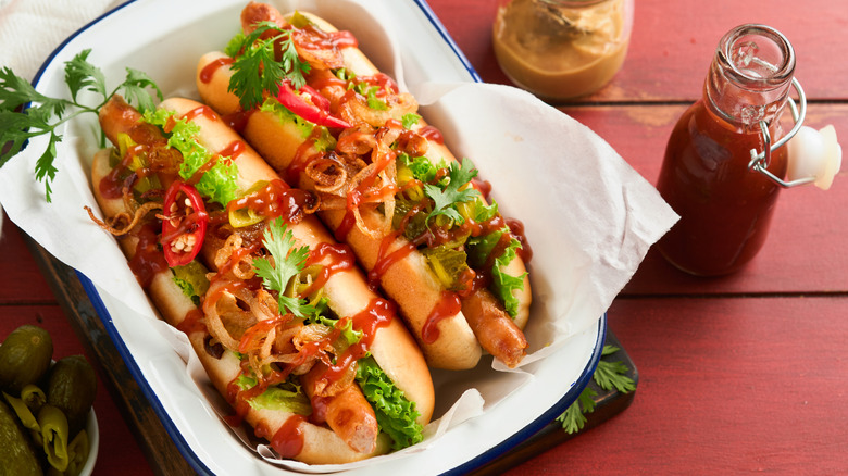 Two hot dogs topped with chili and caramelized onions, next to bottle of hot sauce and cilantro