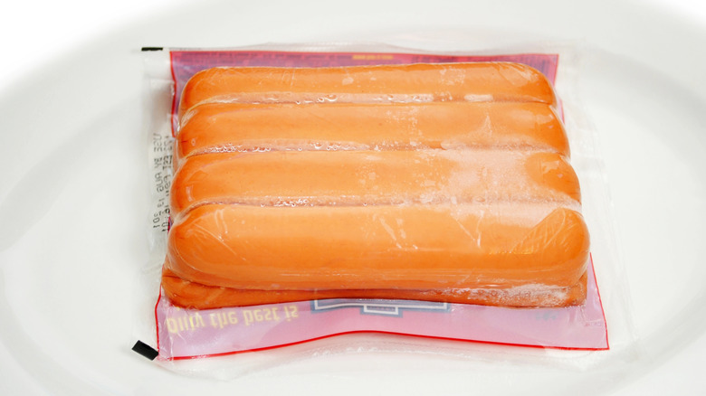 Package of hot dogs thawing on plate