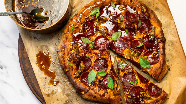 Hot honey pepperoni pizza with a slice taken out beside saucepan with hot honey.