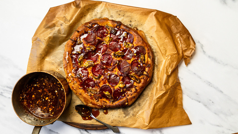 Hot pepperoni pizza on parchment paper beside saucepan with hot honey.