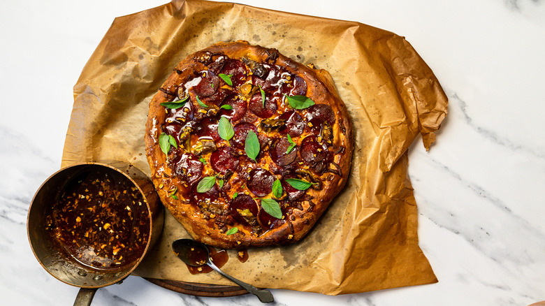 Seasoned and dressed hot honey pepperoni pizza on parchment paper beside saucepan with hot honey.
