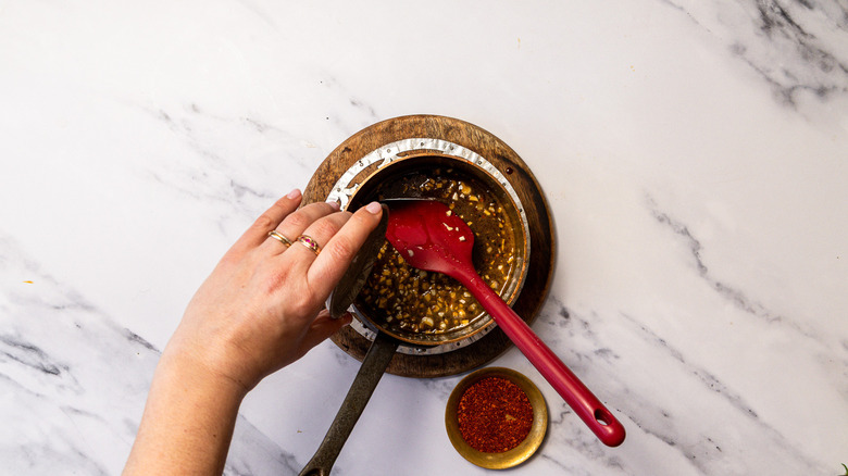 Adding salt and pepper to hot honey in saucepan with spatula.