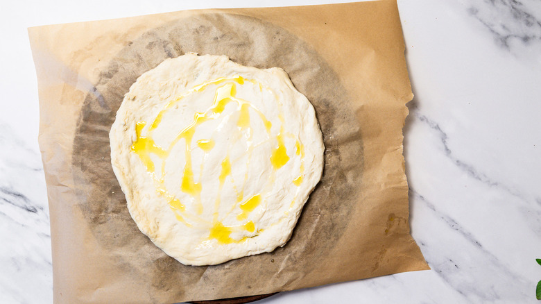 Dough with olive oil spread out on parchment paper.