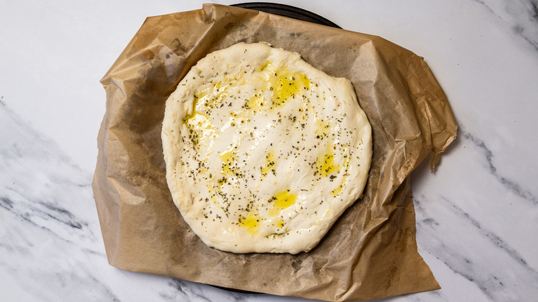 Dough with olive oil and spices spread out on parchment paper.