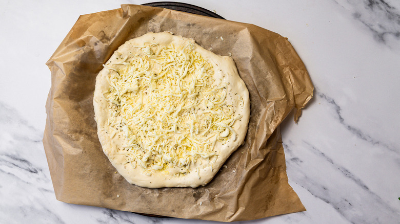 Dough with cheese spread out on parchment paper.
