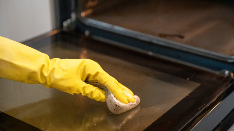Person cleaning oven door with sponge