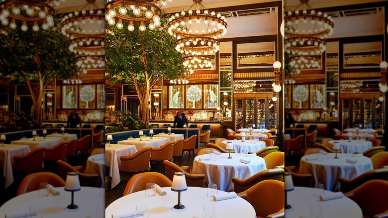 a bar in the background with round tables with white tablecloths and lights on them