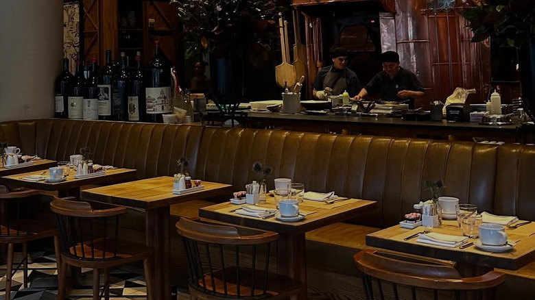 a long, brown booth with chairs and tables and chefs in the back kitchen